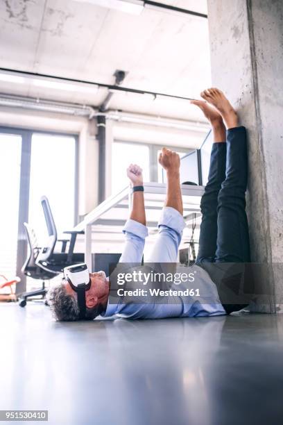 barefoot mature businessman lying on floor in office wearing vr glasses - driving barefoot stock pictures, royalty-free photos & images