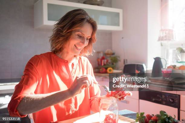 smiling woman making strawberry jam in kitchen at home - marmeladenglas stock-fotos und bilder