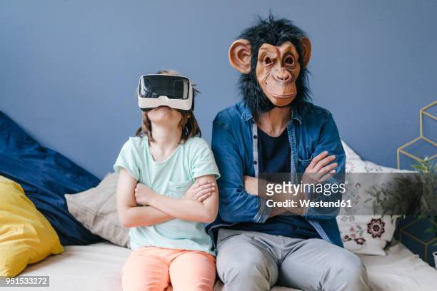 father wearing monkey mask sitting next to son wearing vr glasses at home - monkey wearing glasses stockfoto's en -beelden