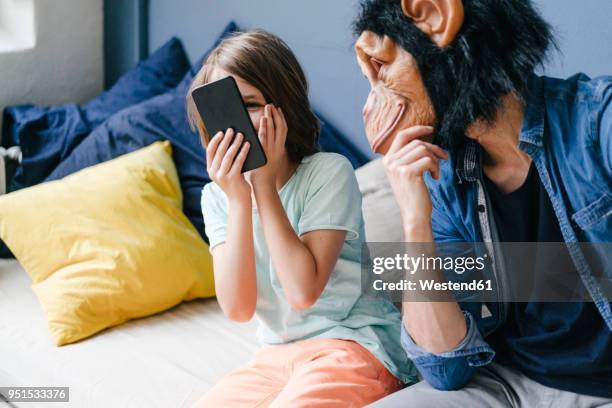 father wearing monkey mask looking at son using smartphone at home - crazy dad stock pictures, royalty-free photos & images