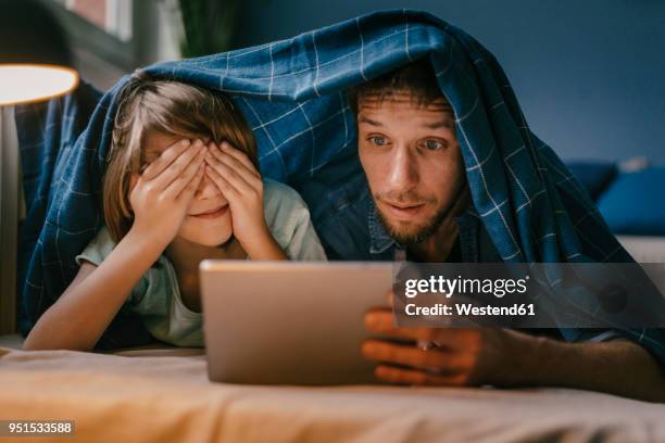 excited father and son watching a movie on tablet under blanket - downloading stock-fotos und bilder