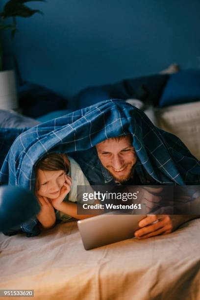 happy father and son watching a movie on tablet under blanket - family home internet stock-fotos und bilder