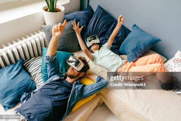 father and son wearing vr glasses lying down at home - famille avec des lunettes de vue photos et images de collection