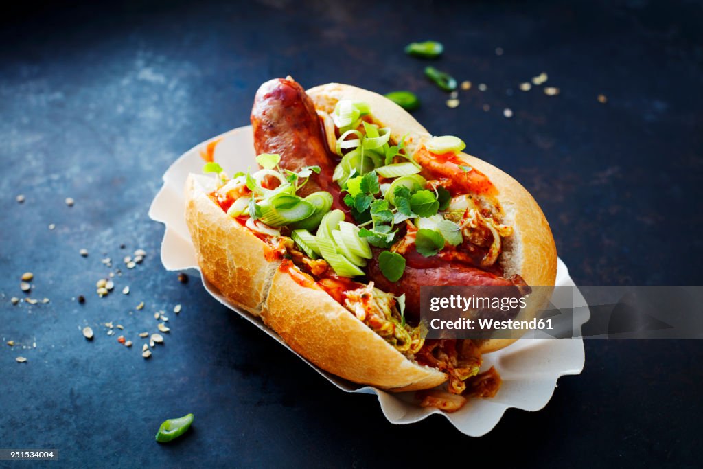 Asian hot dog, fried sausage, spicy chinese cabbage, hot chili sauce, spring onions, cress, bun