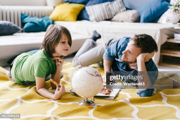 father and son eating pizza next to globe on the floor at home - world children day stock pictures, royalty-free photos & images