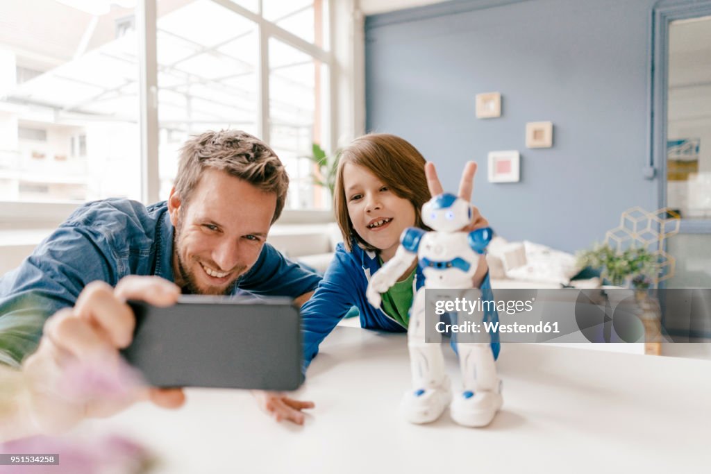 Happy father and son taking a selfie with robot on table at home