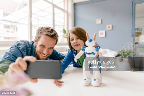 happy father and son taking a selfie with robot on table at home - photo call stock-fotos und bilder