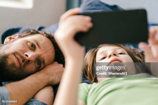 father and son looking at smartphone together at home - media availability stock-fotos und bilder