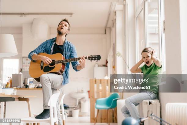 horrified son covering his ears with father playing guitar at home - ungeeignetheit stock-fotos und bilder