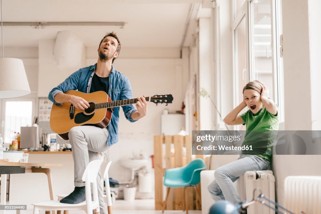 horrified-son-covering-his-ears-with-father-playing-guitar-at-home.jpg