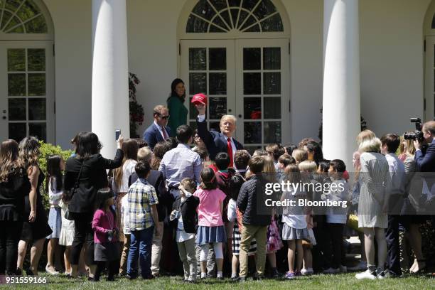 President Donald Trump, center, holds up a "Make America Great Again" hat while greeting White House staff and members of the media's children during...