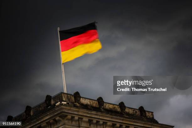 Berlin, Germany The national flag of Germany blows on the Reichstag building in front of a dark cloud sky on April 26, 2018 in Berlin, Germany.