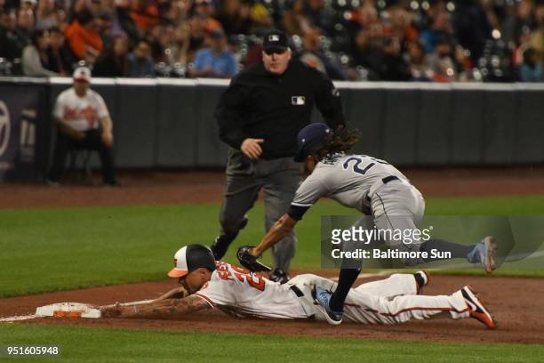 The Baltimore Orioles' Jace Peterson, pursued by Tampa Bay Ray pitcher Chris Archer, steals third base during an infield shift on Chris Davis in the...