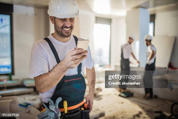jonge gelukkig bouwvakker met behulp van mobiele telefoon tijdens huisvernieuwing. - 2017 common good forum stockfoto's en -beelden