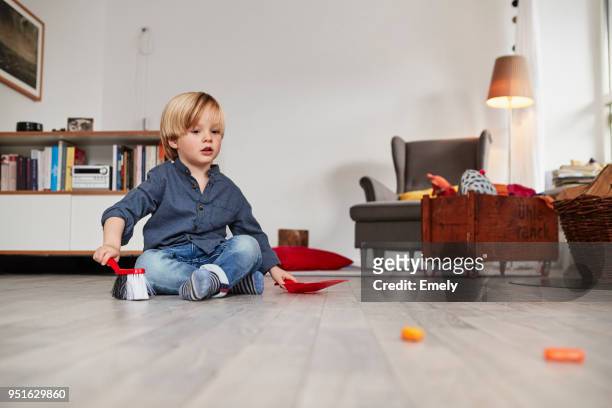 young boy sitting on floor, holding toy dustpan and brush - low angle view room stock pictures, royalty-free photos & images