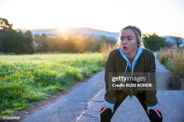 young woman outdoors, taking a break from exercising, hands on knees - exhale stock pictures, royalty-free photos & images