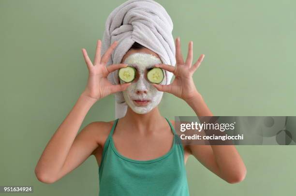 teenage girl with a face mask on holding cucumber slices in front of her eyes - funny facial hair stock pictures, royalty-free photos & images