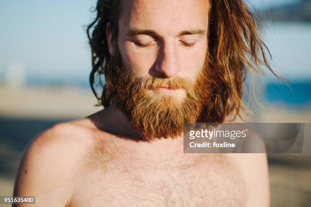 portrait of a man with long hair and a beard standing on beach - hunky guy on beach stock pictures, royalty-free photos & images