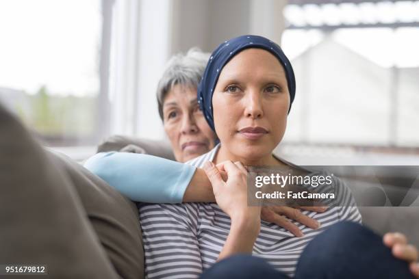 Asian woman in 60s sitting on couch and embracing her mid-30s daughter who is fighting cancer