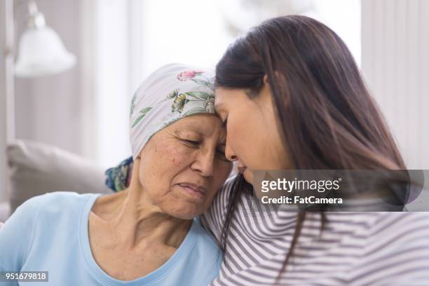 ethnic elderly woman with cancer embracing her adult daughter - cancer illness stock pictures, royalty-free photos & images
