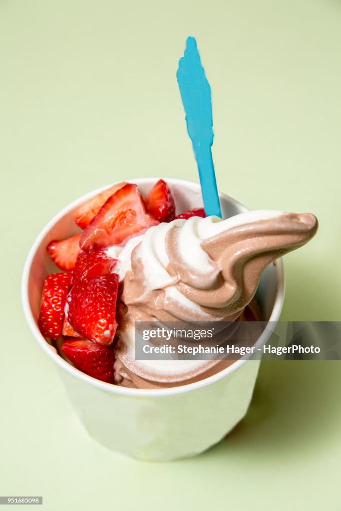 A cup of frozen yogurt with sliced strawberries.