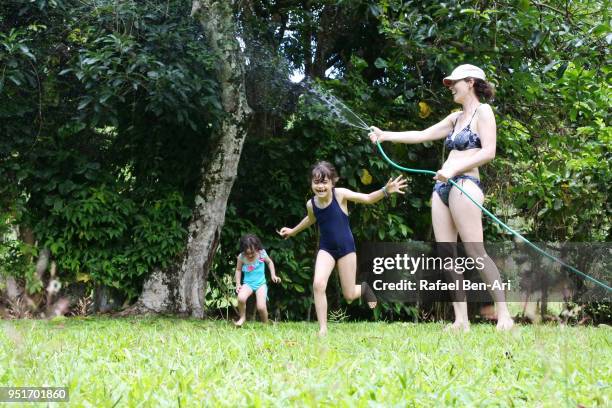 playful young mother spraying water on her two daugthers on a hot summer day - hot polynesian girls stock pictures, royalty-free photos & images