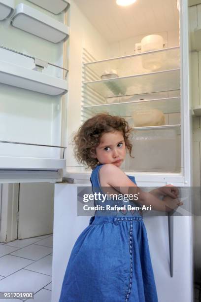 hungry poor little girl looks for food in empty fridge at home - rafael ben ari fotografías e imágenes de stock