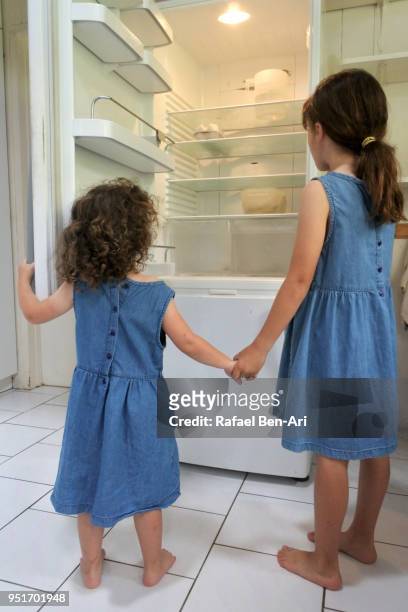hungry poor little sister girls looking for food in empty fridge at home - rafael ben ari fotografías e imágenes de stock