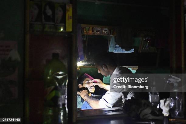 Customer gets a shave at a barber shop illuminated by the torch function of a mobile phone at night in a village on the outskirts of Alwar,...