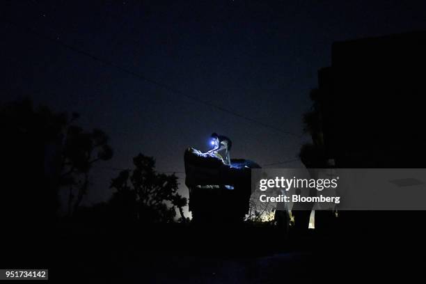 Worker uses the torch function of a mobile phone as he unloads stacks of hay from a tractor trailer at night in a village on the outskirts of Alwar,...