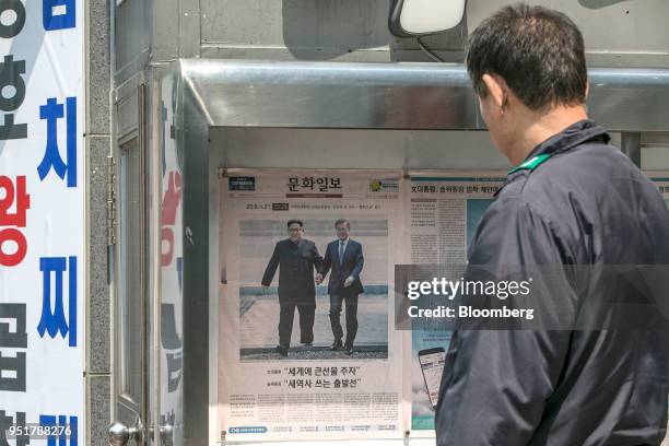 Man looks at a copy of Munhwa Ilbo newspaper, featuring photographs of Moon Jae-in, South Korea's President, right, and Kim Jong Un, North Korea's...