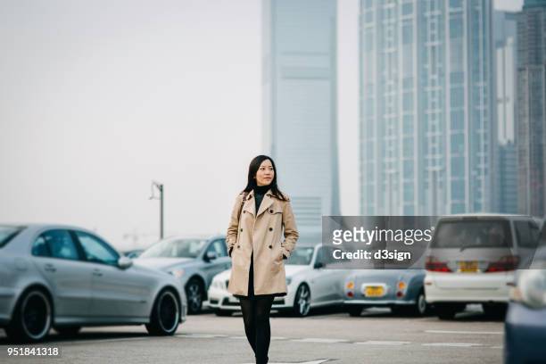 young asian woman standing against cityscape and looking away with confidence - busy park stock pictures, royalty-free photos & images