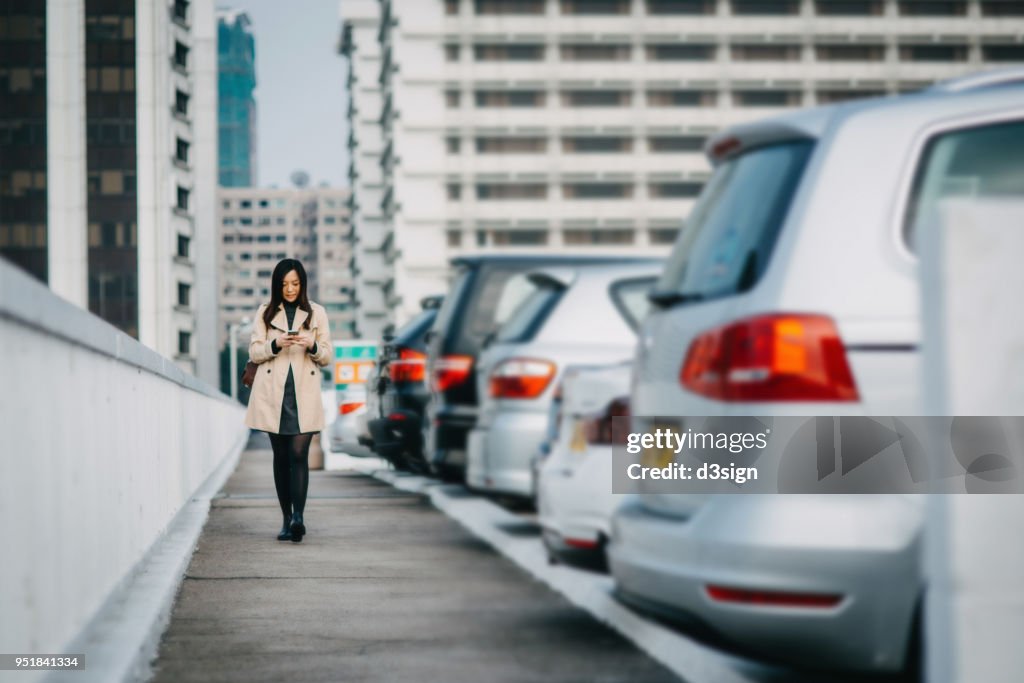Busy businesswoman reading emails on smartphone in rooftop car park in city