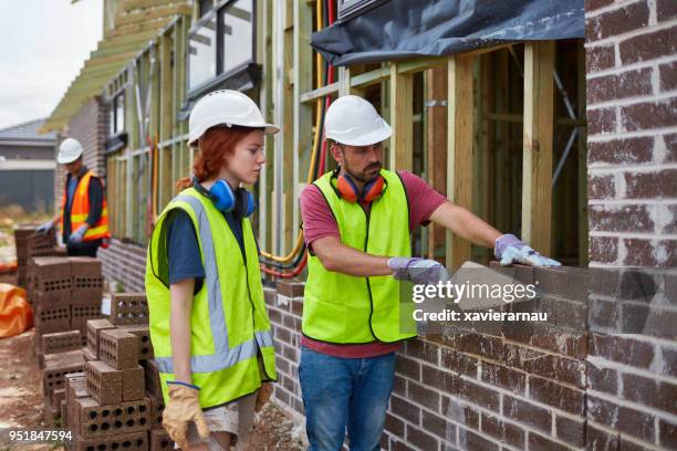female trainee looking at worker building wall - female bricklayer stock pictures, royalty-free photos & images