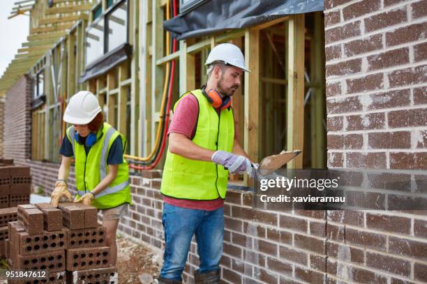 maurer zementieren ziegel mit auszubildenden am standort - brick layer stock-fotos und bilder