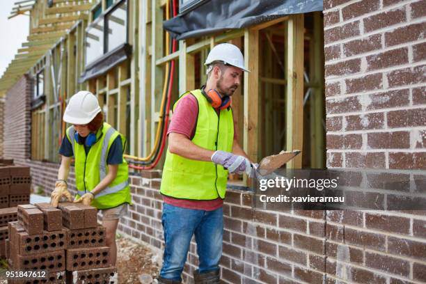 bricklayer cementing bricks with trainee at site - female bricklayer stock pictures, royalty-free photos & images