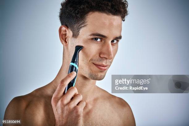handsome young man trimming sideburns with a beard trimmer - sideburn stock pictures, royalty-free photos & images