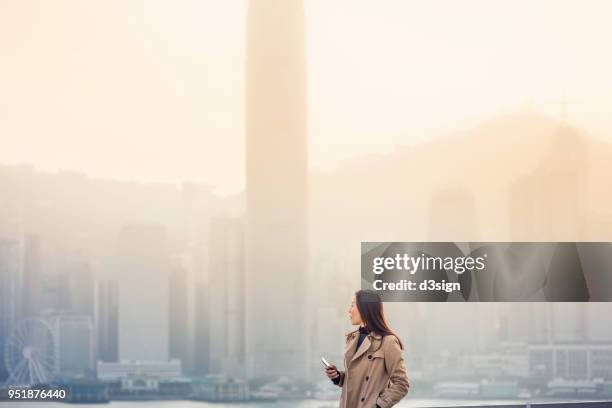 young businesswoman looking towards city skyline with confidence - asian woman smiling sunrise stock-fotos und bilder