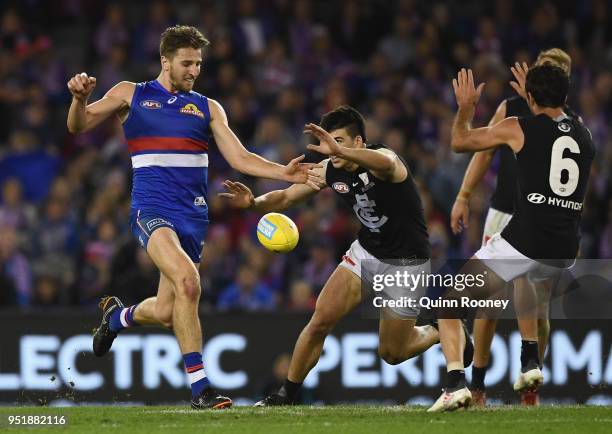 Marcus Bontempelli of the Bulldogs kicks whilst being tackled by Matthew Kennedy of the Blues during the AFL round six match between the Western...