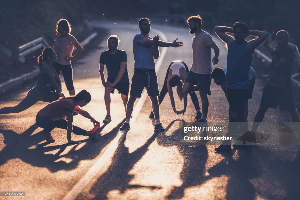 Large group of marathon runners warming up on a road at sunset.