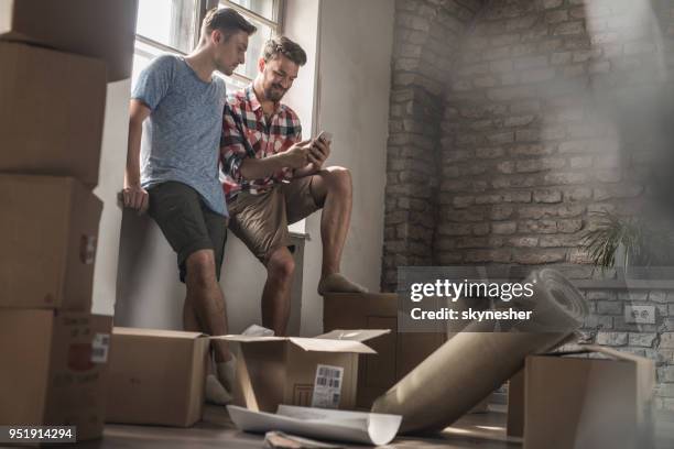 jeunes hommes gais lire un sms sur téléphone portable tout en se déplaçant dans la nouvelle maison. - sms'en photos et images de collection