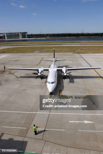 Marshaller with bats controlling CityJet Fokker F-50 taxiing at London City.