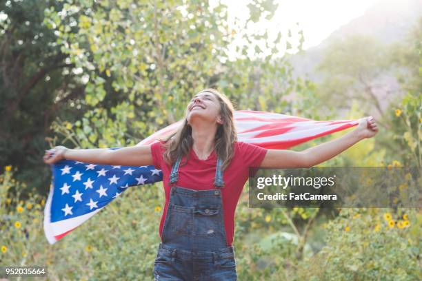 a young brunette woman holds an american flag up behind her - small town parade stock pictures, royalty-free photos & images