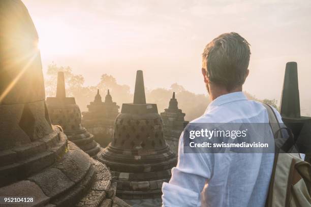 travel man contemplates sunrise at borobudur temple, indonesia - borobudur temple stock pictures, royalty-free photos & images
