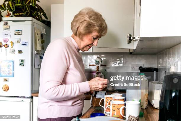 senior woman making mugs of coffee in her kitchen - widow pension stock pictures, royalty-free photos & images