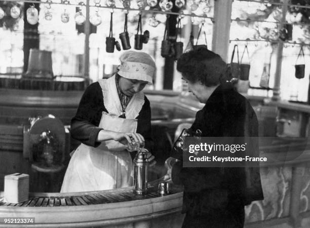 Une femme mesure et embouteille l'eau de Vichy dans les thermes pour une cliente, circa 1930 à Vichy, France.