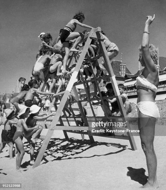 Des enfants s'amusent et pratiquent des activités sportives sous la direction de leur monitrice sur la plage le 6 août 1949 à La Baule, France.