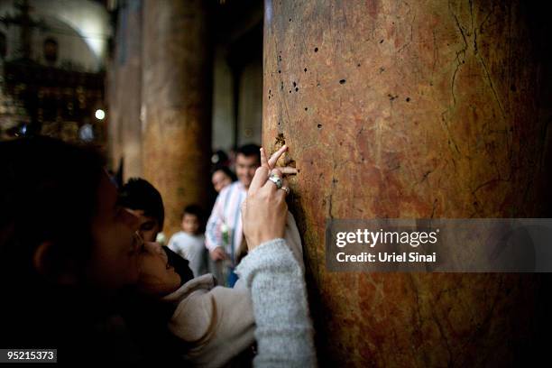 Woman helps her child to places her fingers into the crucifix-shaped holes in one of the ancient columns in the Church of the Nativity, as Christians...