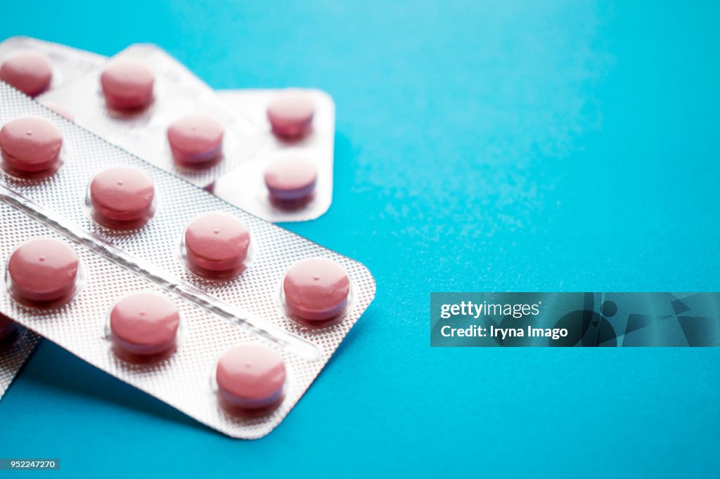 Close up of statin tablet or generic pill in silvery blisters on blue background