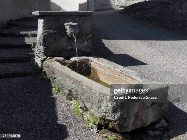 ancient fountain in giumaglio, decorated with granite human head sculpture - giumaglio stock pictures, royalty-free photos & images